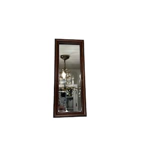 May include: A rectangular, dark brown framed mirror. The mirror reflects a room with a chandelier and other objects. The frame has a simple, classic design. The mirror is vertically oriented.