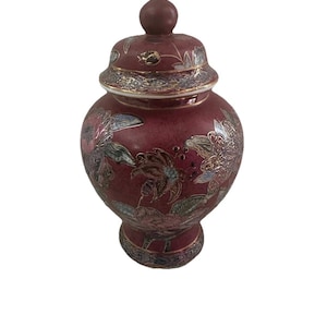 Peut inclure: Un pot en céramique marron avec un couvercle, orné de motifs floraux argentés et dorés. Le pot a une forme arrondie et un couvercle avec un petit bouton. Les motifs floraux sont détaillés et couvrent la surface du pot. Mesures en centimètres.
