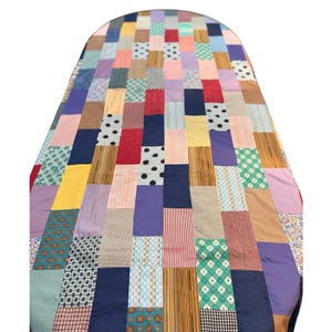 May include: A rectangular quilt featuring a patchwork design composed of numerous vertical fabric strips. The textile displays a diverse array of colours including yellow, blue, red, green, purple, and brown, with various patterns like polka dots, stripes, and floral prints.
