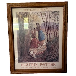 以下が含まれることがあります： ビクトリア・ポッターの「Mr. Todの物語」の額入りプリント。森の中で2匹のウサギを描いたアートワークで、上下にテキストが入っています。フレームはミディアムブラウンです。