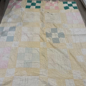 Può includere: Una trapunta fatta a mano con un design patchwork. La trapunta presenta un motivo a griglia di quadrati color crema, bianco, rosa, verde e blu. La trapunta sembra essere fatta di cotone e ha un'estetica vintage.