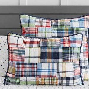 May include: Two patchwork pillow shams with a variety of plaid patterns in red, blue, green, and yellow. The shams have a dark blue trim and are placed on a bed with a gray headboard. The patchwork design adds a rustic touch to the bedding.
