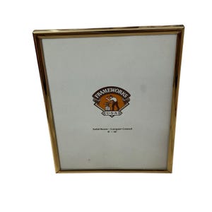 May include: A gold-colored, rectangular picture frame with a white interior. The frame has a brass finish and the text "FRAMEWORKS U.S.A." is visible. The frame is 8 x 10 inches.