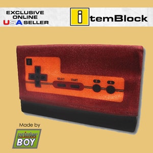 Puede incluir: Una cartera roja y negra con una imagen impresa de un mando de videojuego clásico. El mando es naranja y tiene las palabras "Select", "Start", "B" y "A" impresas en él. La cartera está hecha por "printer BOY".