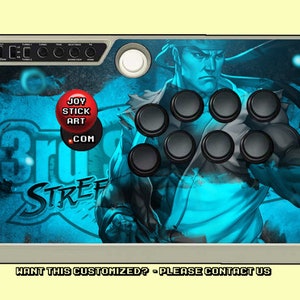 May include: A gray arcade joystick with a blue and white design featuring a character from Street Fighter. The design includes the text "Joy Stick Art .com" and "Street Fighter".