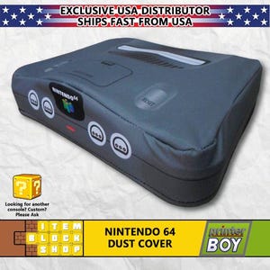 May include: A gray Nintendo 64 console dust cover with the words "NINTENDO 64" printed on the top. The cover has a textured fabric finish and features a reset button and four controller ports. The words "DUST COVER" are printed in yellow on a black background below the console.