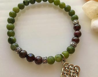May include: A green and burgundy beaded bracelet with a silver Celtic knot charm. The bracelet is made with natural stones and features a silver accent bead between each stone.
