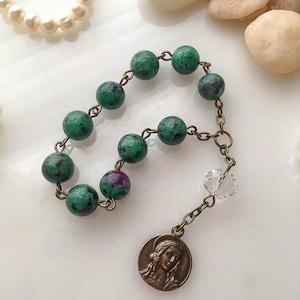 May include: A green gemstone rosary bracelet with a clear crystal charm and a bronze pendant featuring a religious image.