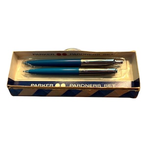 May include: A vintage Parker Pardners Set in its original box. The set includes a blue ballpoint pen and a matching fountain pen with silver accents. The box is a light tan with blue and white stripes and the words "PARKER" and "PARDNERS SET".