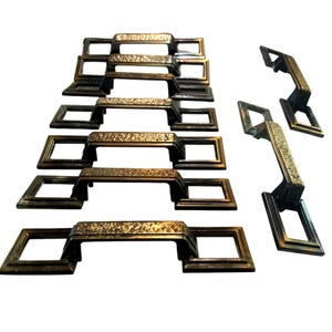 May include: Set of eight antique brass cabinet pulls with a textured finish. The pulls have a square shape with a rounded handle.