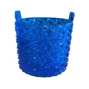 以下が含まれることがあります： 鮮やかな青色のガラス容器で、テクスチャ加工された幾何学模様が施されています。容器には2つの小さなハンドルと円筒形があります。ガラスは多面的なデザインで、きらめく効果を生み出しています。この装飾品は、花瓶や収納容器として使用できます。