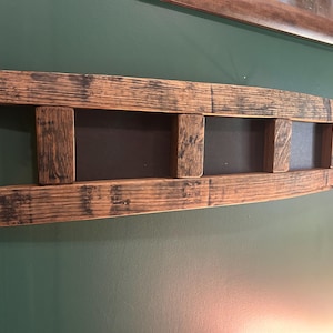 May include: A horizontal wall-mounted rack constructed from two curved wooden barrel staves connected by four vertical wooden slats, featuring a dark brown finish with visible wood grain and charred, weathered textures throughout the surface.