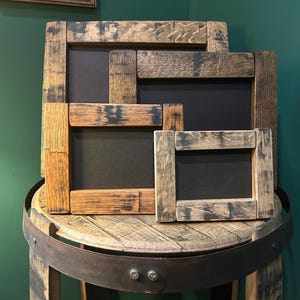 May include: A set of four rectangular picture frames constructed from reclaimed wood with a weathered, dark brown finish. Each frame features a thick, textured border and a solid black interior panel, arranged in a stacked, overlapping formation.