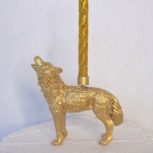May include: A gold-colored wolf figurine candle holder with a tall, glittery gold candle. The wolf is in a howling pose. The candle is approximately 8 inches tall.