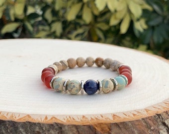 Puede incluir: Un brazalete de cuentas multicolores con cuentas rojas, marrones, azules y verdes. El brazalete tiene separadores de metal plateado entre las cuentas.