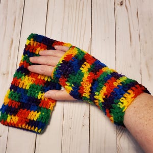 May include: Rainbow striped crochet fingerless gloves. The gloves are made with a variety of colors, including red, orange, yellow, green, blue, and purple.