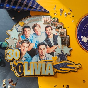 May include: A blue and yellow cake topper with the number 30 and the name Olivia. The topper features a collage of photos of the boy band *NSYNC.