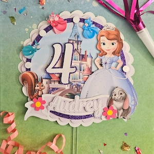 May include: A purple and white cake topper featuring a princess character with a crown, a squirrel, a rabbit, and the number 4. The topper also includes the name "Audrey" in purple glitter letters.