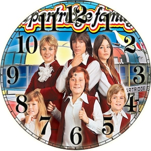 May include: A vintage clock featuring the cast of the Partridge Family television show. The clock face is a colorful illustration of a bus with the numbers 1 through 12 around the edge. The cast members are depicted in their signature outfits, with the words "Partridge Family" in a yellow and red font.