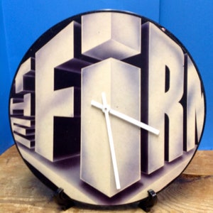 May include: A black vinyl record clock with white hands and the word "FIRN" in white letters on a purple background.