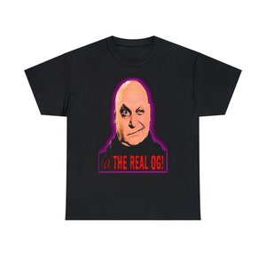 May include: Black t-shirt featuring a cartoon image of a bald man with a mischievous grin. The text "@THE REAL OG!" is printed in red on a purple background below the image.