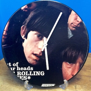 May include: A black vinyl record clock featuring a close-up image of the Rolling Stones band members. The clock hands are white and the record has the text "Out of Our Heads The Rolling Stones*" printed on it.