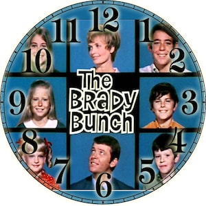 May include: A blue and black clock with a white background featuring the cast of The Brady Bunch. The clock face has the Brady Bunch logo and each number is surrounded by a photo of a different cast member.