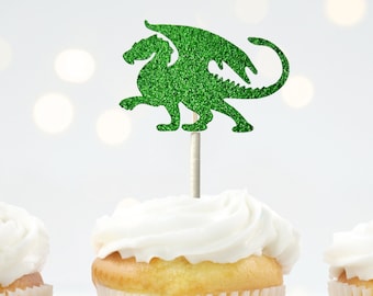 May include: Green glitter dragon cupcake topper. The dragon is standing on its hind legs with its wings spread out. The topper is on a white cupcake with white frosting.