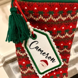 Puede incluir: Calcet&iacute;n de Navidad rojo y verde con una etiqueta blanca que dice "Cameron" y un borla verde.