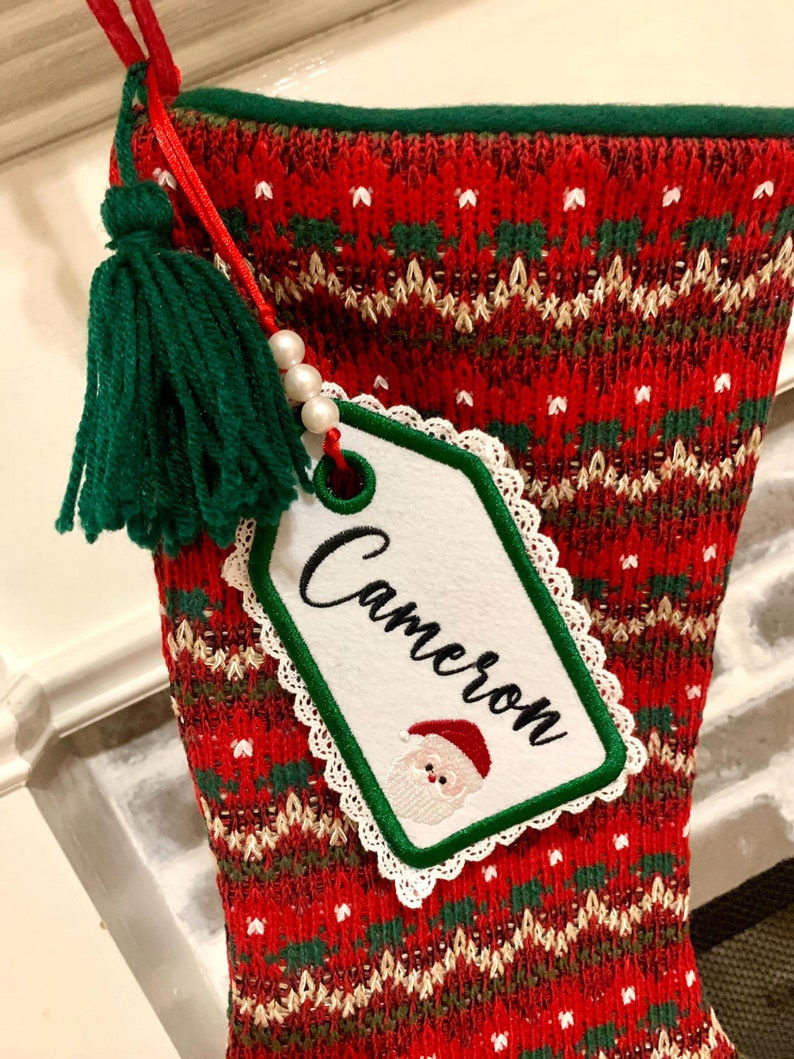 Puede incluir: Calcet&iacute;n de Navidad rojo y verde con una etiqueta blanca que dice "Cameron" y un borla verde.