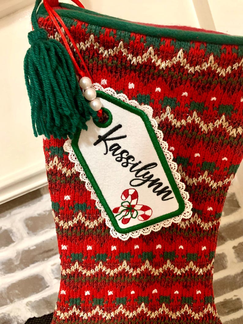 Puede incluir: Calcet&iacute;n de Navidad de punto rojo y verde con una etiqueta blanca que dice "Kassilynn" y un borla verde.