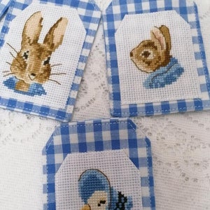 Può includere: Tre etichette regalo in tessuto vichy blu e bianco con immagini ricamate di Peter Rabbit e un'anatra. Le etichette sono perfette per aggiungere un tocco di fantasia ai regali.