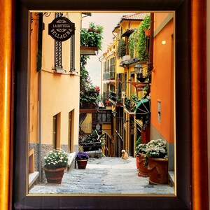 May include: A narrow, cobblestone alleyway in a European city with colorful buildings and potted plants. The sign above the entrance reads "La Bottega Bellatina".