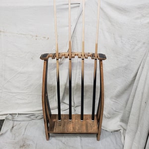 May include: A wooden pool cue rack made from a reclaimed wine barrel with five pool cues resting in the rack. The rack has a dark brown stain and is made of wood with a rustic finish.