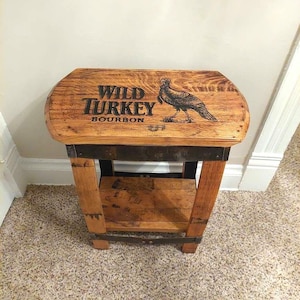 May include: A small, wooden side table with a Wild Turkey Bourbon logo and a turkey illustration. The table has a shelf and is supported by four legs. The wood has a natural finish and is accented with metal bands.