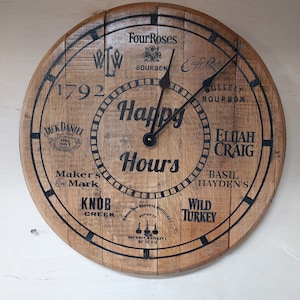 Könnte beinhalten: Ein hölzernes Zifferblatt mit schwarzen Markierungen und einem schwarzen Uhrzeiger. Das Zifferblatt ist mit den Namen verschiedener Bourbon-Marken verziert, darunter Jack Daniel's, Maker's Mark, Four Roses, Wild Turkey und Knob Creek. Das Zifferblatt enthält auch den Text "Happy Hours" und "1792".