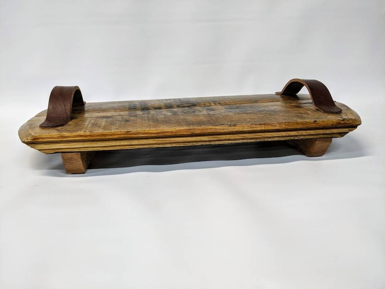 May include: A rustic wooden serving tray with two brown leather handles. The tray has a natural wood finish and is made of reclaimed wood.