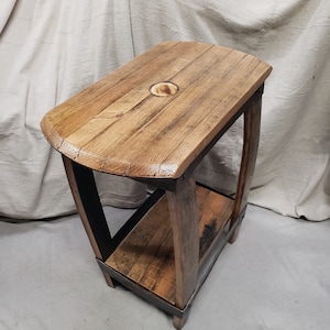 May include: A rustic wooden side table with a rectangular top and a lower shelf. The table is constructed from reclaimed wood with visible grain and a natural finish. The legs are supported by metal bands.