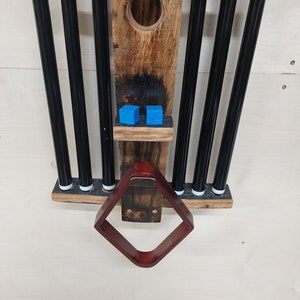 May include: A wooden pool cue rack with six black pool cues and a brown leather rack. Two blue pool balls are on a shelf above the rack.