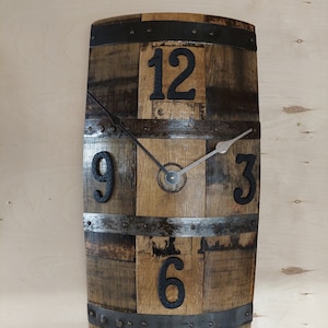 May include: A rustic wooden clock with black metal accents and Roman numeral markings. The clock is made from a repurposed barrel stave and has a distressed wood finish.