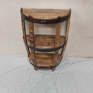 May include: A wooden shelf unit made from reclaimed wine barrels. The shelf has three tiers and is finished in a natural wood stain. The shelf is a half-circle shape and is perfect for displaying decorative items or storing small items.