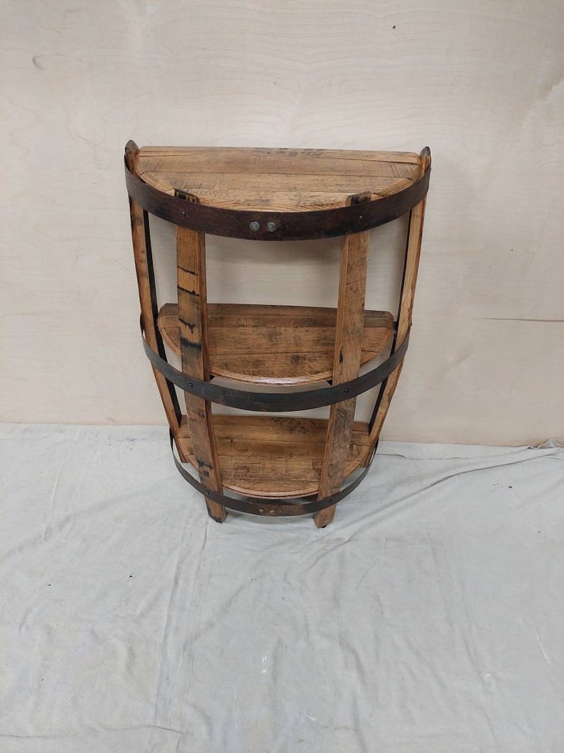 May include: A wooden shelf unit made from reclaimed wine barrels. The shelf has three tiers and is finished in a natural wood stain. The shelf is a half-circle shape and is perfect for displaying decorative items or storing small items.