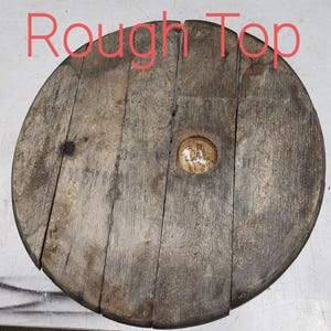 May include: Rough Top is written on a wooden round disc with a hole in the center. The disc is made of wood planks and has a rustic, weathered look.
