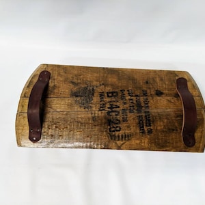 May include: A wooden serving tray made from a repurposed whiskey barrel with two leather handles. The barrel has the text "WM.  REAMS & SONS, INC.  LOUISVILLE, KY.  DIST. BY  NATIONAL DISTILLERS PRODUCTS CO.  P.O. BOX 1230  N.Y.C.  TANK 221  B14C28" printed on it.