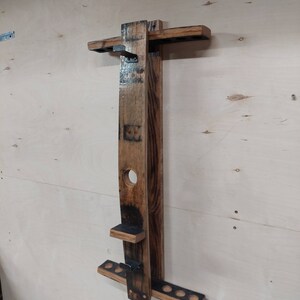 May include: A wooden wall-mounted rack made from reclaimed wine barrels, featuring a shelf and multiple hooks for hanging items. The rack has a dark brown stain and a distressed finish.