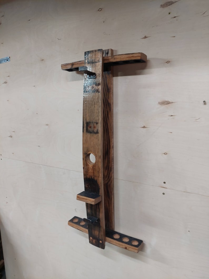 May include: A wooden wall-mounted rack made from reclaimed wine barrels, featuring a shelf and multiple hooks for hanging items. The rack has a dark brown stain and a distressed finish.