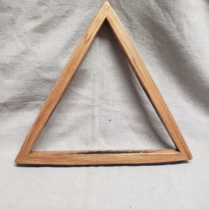May include: A wooden triangle rack for pool balls. The rack is made of light brown wood with a dark brown stain. The rack is designed to hold the balls in a triangular shape.
