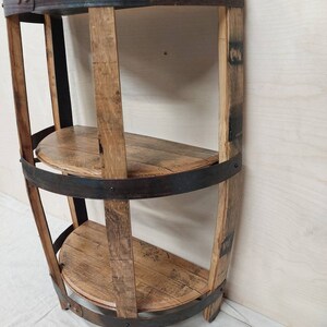 May include: A three-tiered shelf unit made from reclaimed wood barrel staves and metal bands. The shelves are curved and the unit has a rustic, industrial look.