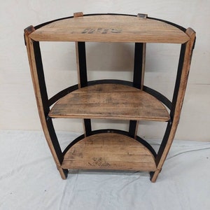 May include: A three-tiered corner shelf made from reclaimed wood with black metal accents. The shelves are curved and have a rustic look.