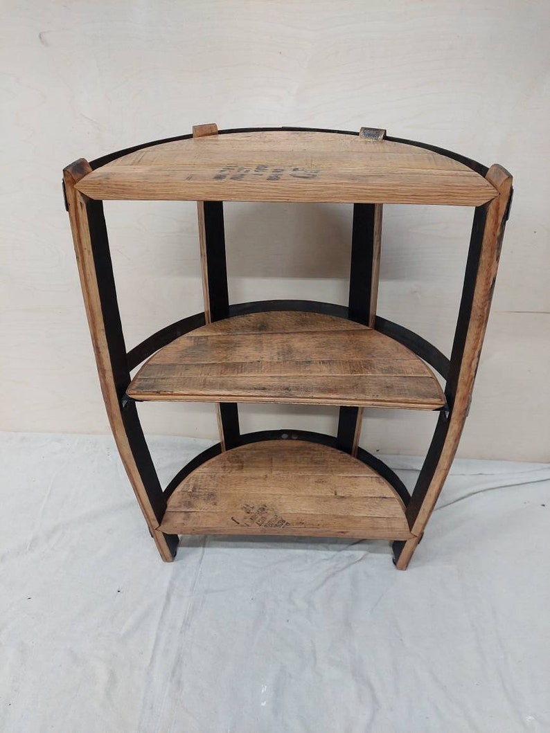 May include: A three-tiered corner shelf made from reclaimed wood with black metal accents. The shelves are curved and have a rustic look.